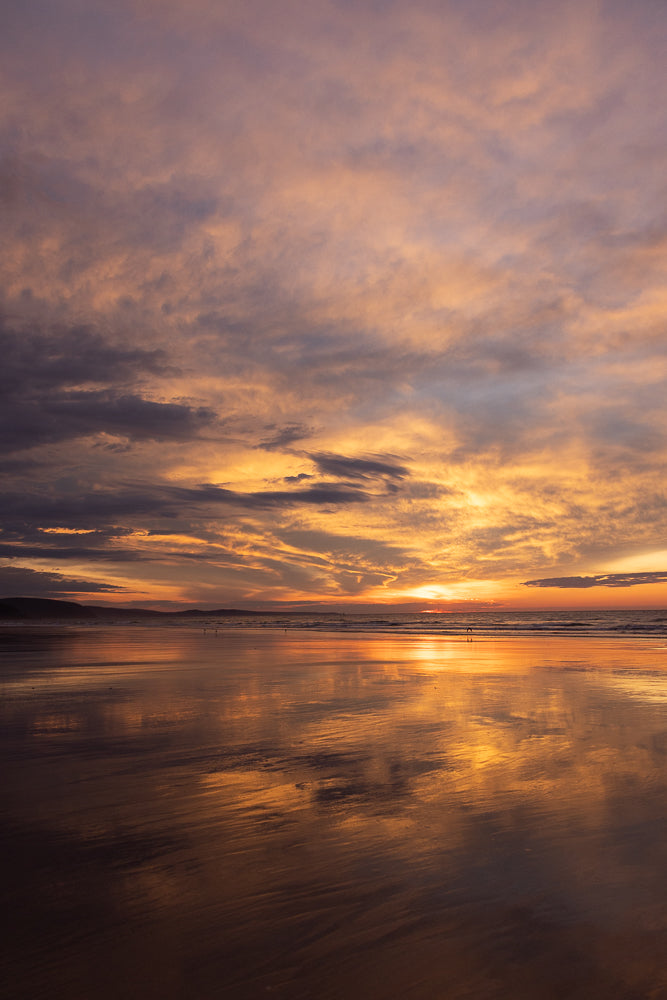 Soft red, purple and orange sunset over a quiet beach with reflections on the wet sand