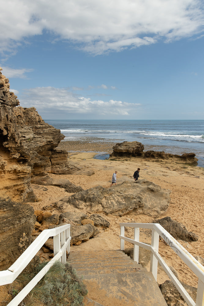 2 teenagers walking on rocky beach with white stairs leading to them