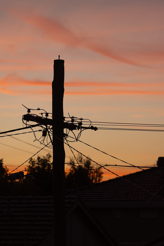 Silhouette of a telephone pole with wires against a sunset sky with orange and pink clouds.