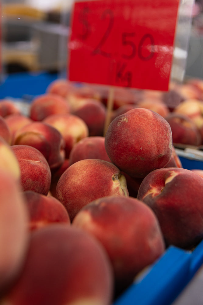 A close-up shot of ripe peaches for sale at a market. A red sign in the background reads "$2.50 / kg".