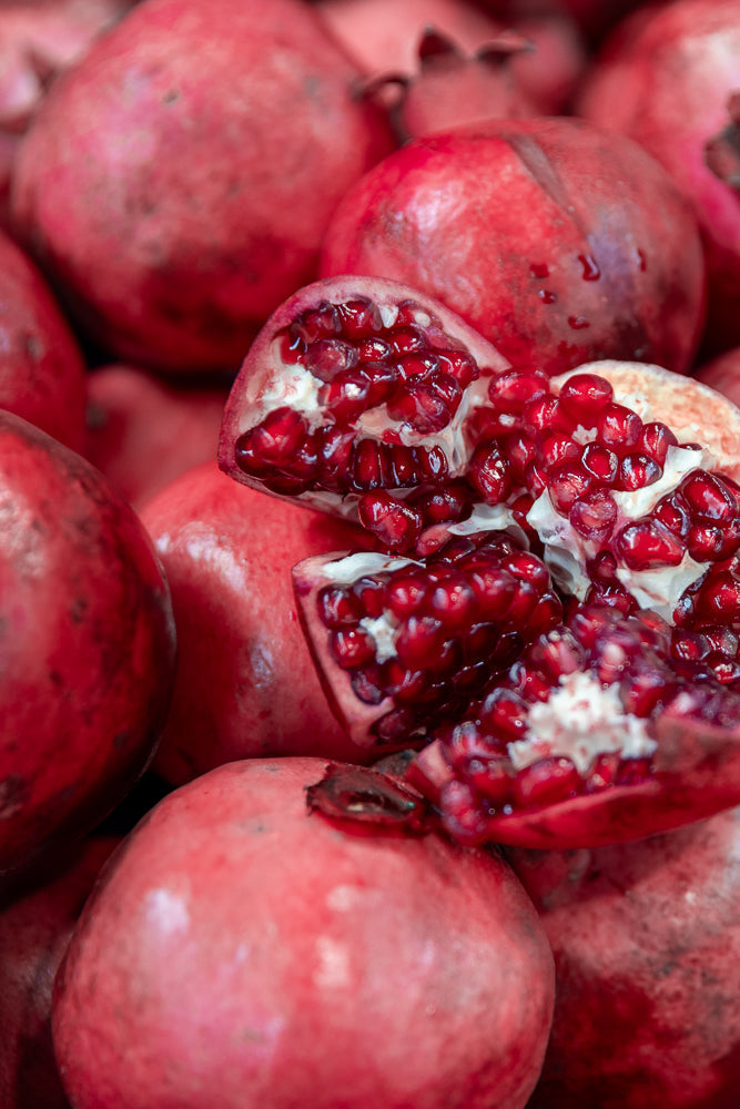 A close-up shot of a pile of ripe pomegranates, with one pomegranate split open to reveal its juicy, red arils.