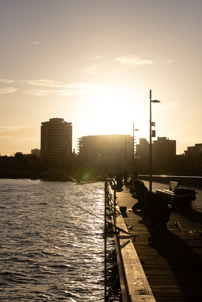 Silhouette people fishing at sunset on a pier with buildings in background