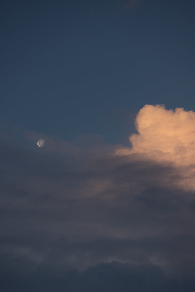 A full moon is visible in the dark blue sky, partially obscured by clouds. A large, fluffy cloud with a warm, orange glow is on the right side of the image.