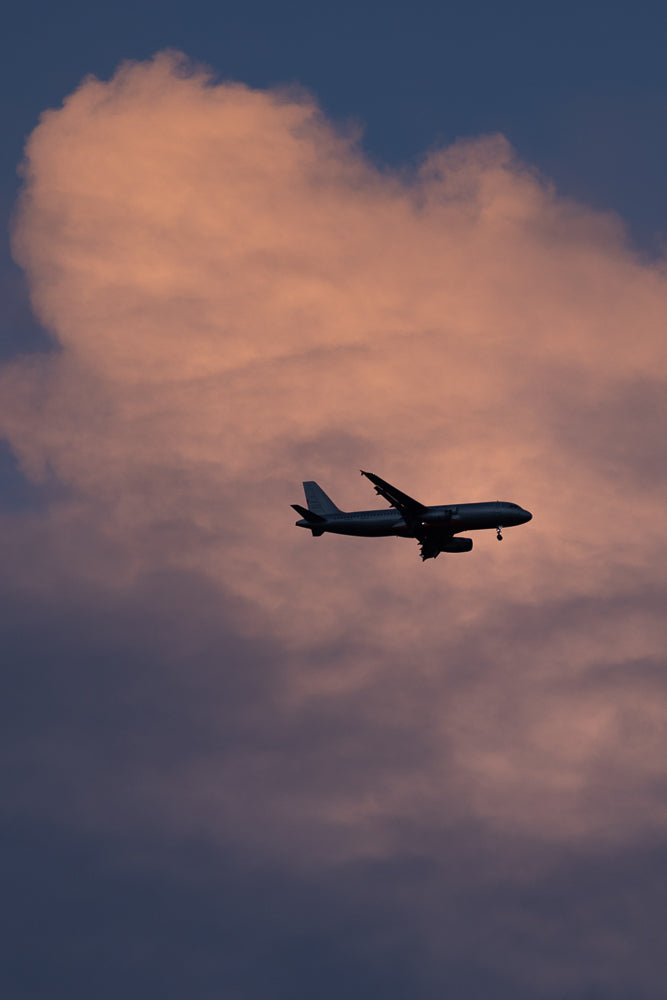 A silhouetted airplane flies through a dusky sky filled with soft, pinkish-orange clouds.