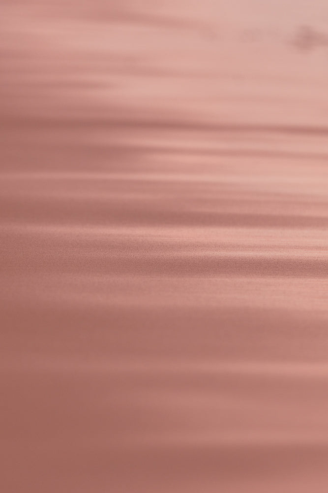 A soft focus, abstract background with horizontal lines of light and shadow in shades of rose gold and pink. The texture appears slightly grainy, creating a subtle, shimmering effect.