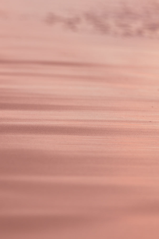 A soft focus, abstract background with horizontal lines of light and shadow in shades of rose gold and pink. The texture appears slightly grainy, creating a subtle, shimmering effect.