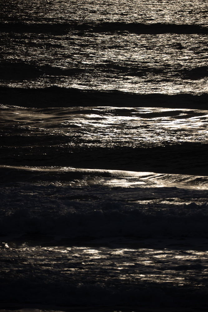 The dark, choppy ocean surface reflects the bright sunlight, creating shimmering lines of light across the water. The waves are small and close together, with the light catching the crests of the waves.