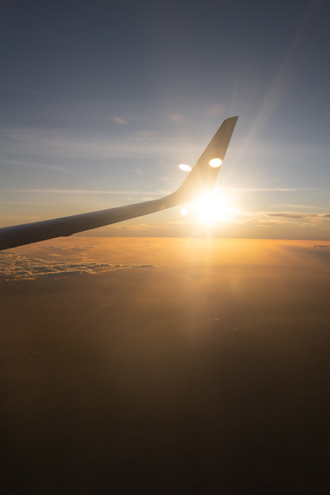 View from an airplane window at sunset. The sun is shining brightly, casting rays of light through the clouds and illuminating the airplane's wing.