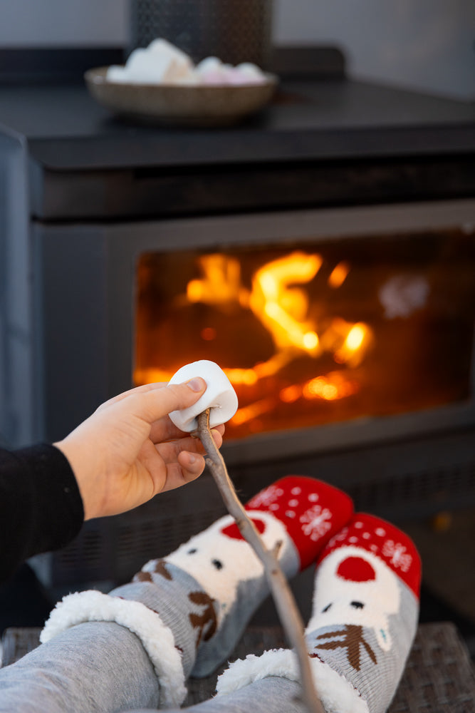 A person wearing festive socks roasts a marshmallow over a fireplace.