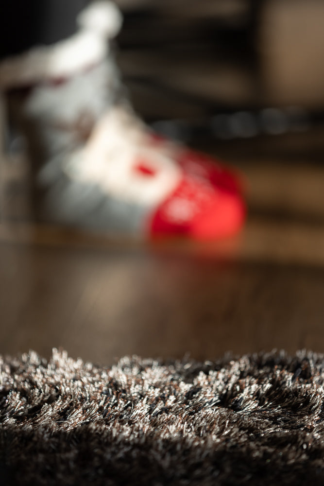A close-up, low-angle shot of a fluffy, brown and white shag rug in the foreground. In the blurred background, a person's foot wearing a red and white sneaker is visible.