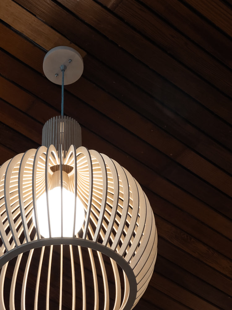A modern, spherical pendant light fixture made of light-colored wood slats hangs from a white ceiling mount against a dark wood paneled ceiling.
