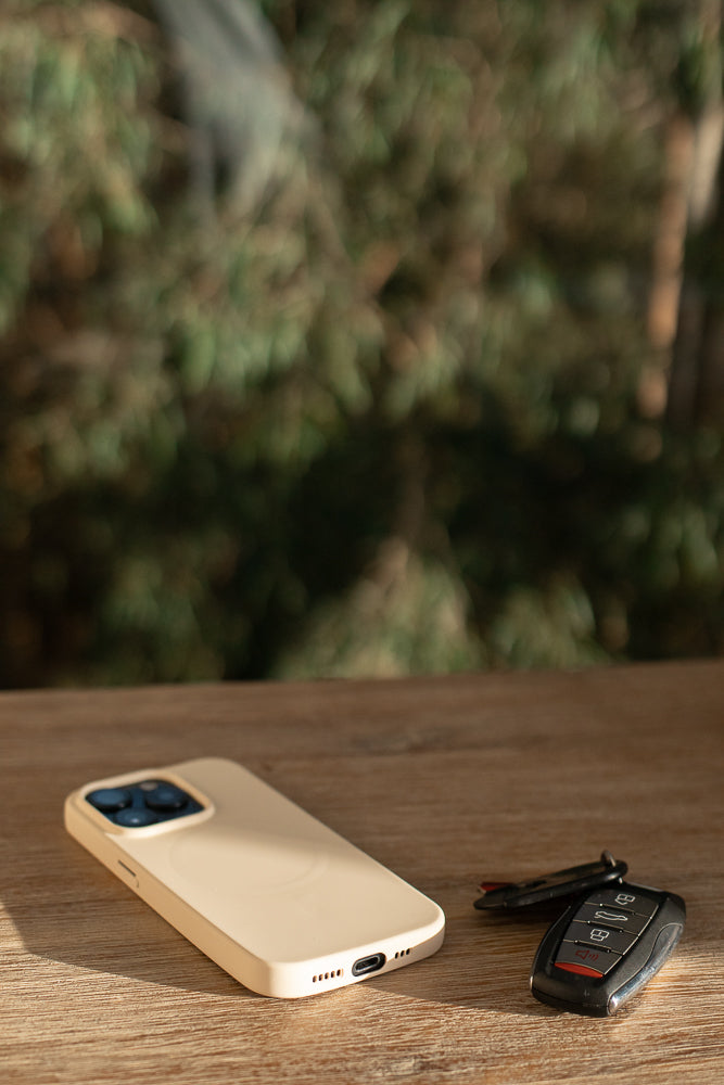 A light beige smartphone and a car key fob rest on a wooden surface. The phone is positioned to the left, with its camera array visible. The key fob, with multiple buttons, is to the right of the phone.