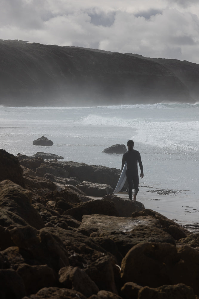 Surfer walk across rocks to get to beach