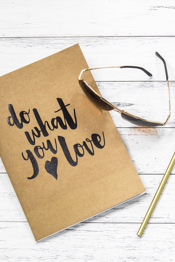 A brown notebook with the phrase "do what you love" written in black calligraphy. A pair of gold-rimmed sunglasses rests on top of the notebook, and a gold pen lies to the right.