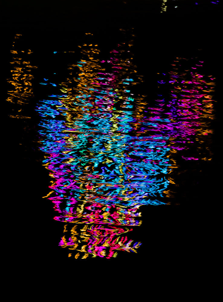 Abstract image of blurred, colorful lights against a black background. The lights are streaks of blue, pink, yellow, and orange, creating a vibrant, energetic pattern.