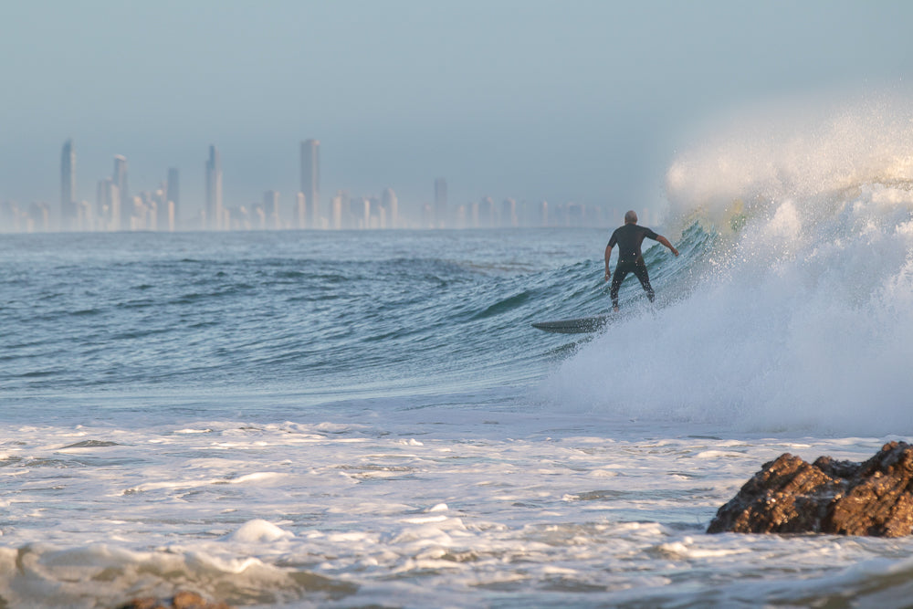 Surfer riding wave with Gold Coast skyline in the background