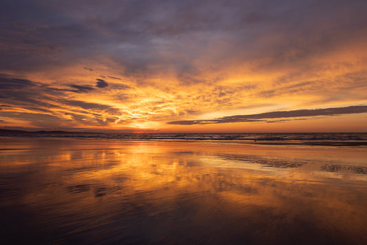 Bright red, purple and orange sunset over a tranquil beach with reflections on the wet sand