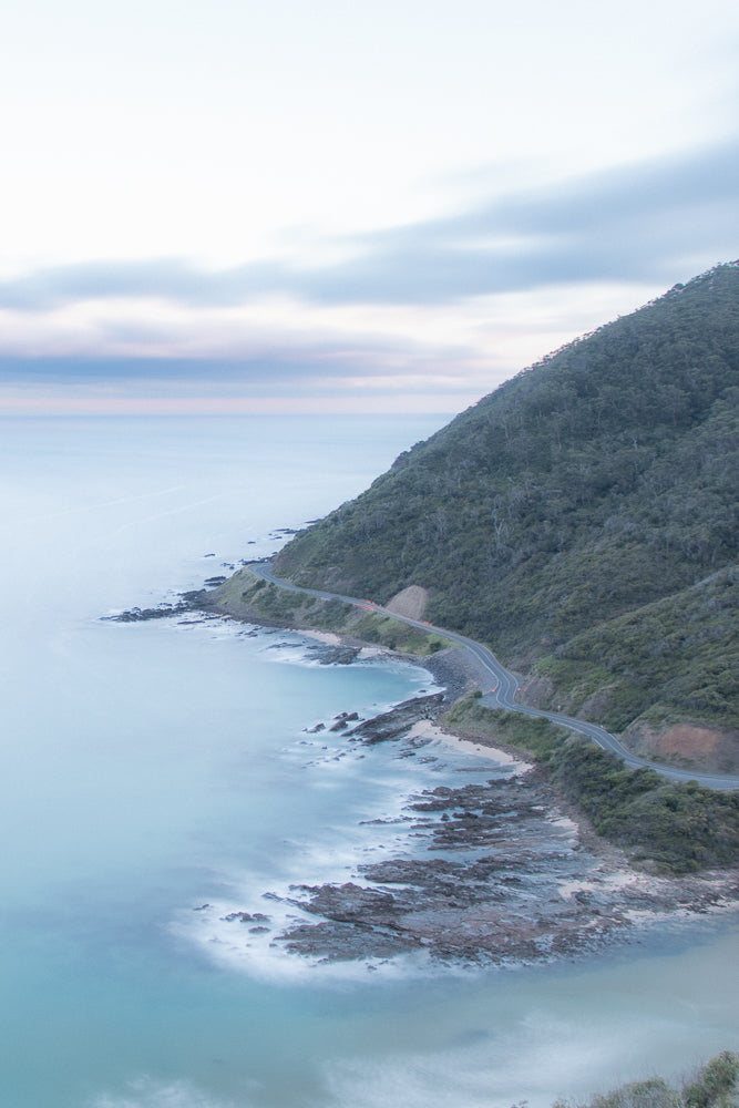 A serene aerial view of Great Ocean Road, clouds and sky at sunset, with soft pink and blue hues blending into the vast expanse.