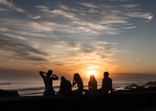 Silhouetted group of people watching sunset by the ocean