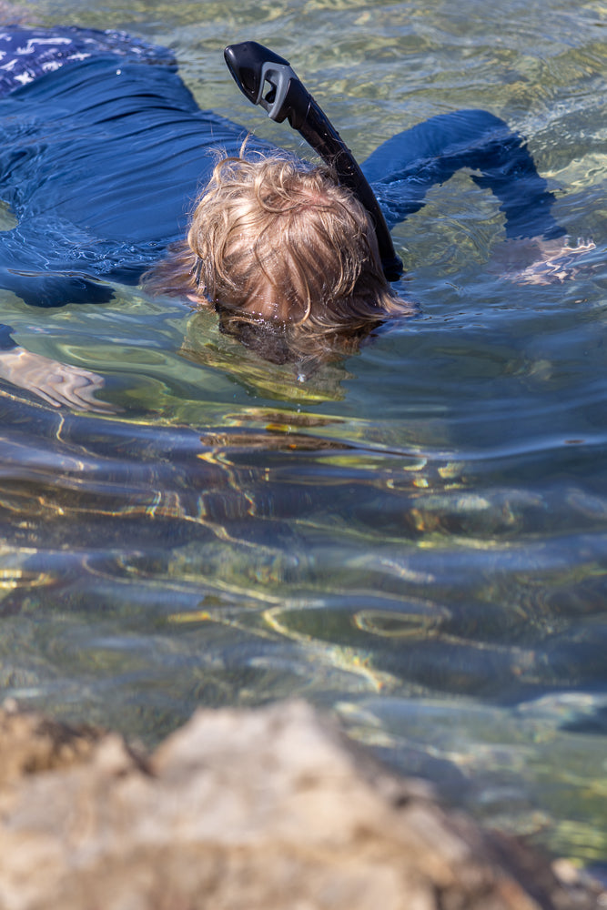 Boy Snorkeling in clear water in rock pool in blue rashie and blue shorts