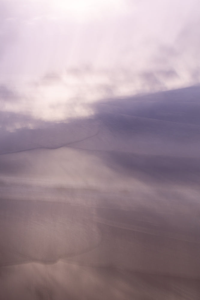 Abstract image of sand dunes with soft, diffused light creating a dreamy, ethereal atmosphere. The colors are muted purples and pinks, with subtle shadows and highlights.