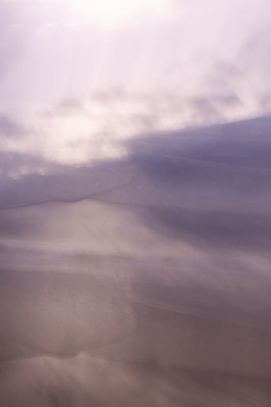 Abstract image of sand dunes with soft, diffused light creating a dreamy, ethereal atmosphere. The colors are muted purples and pinks, with subtle shadows and highlights.