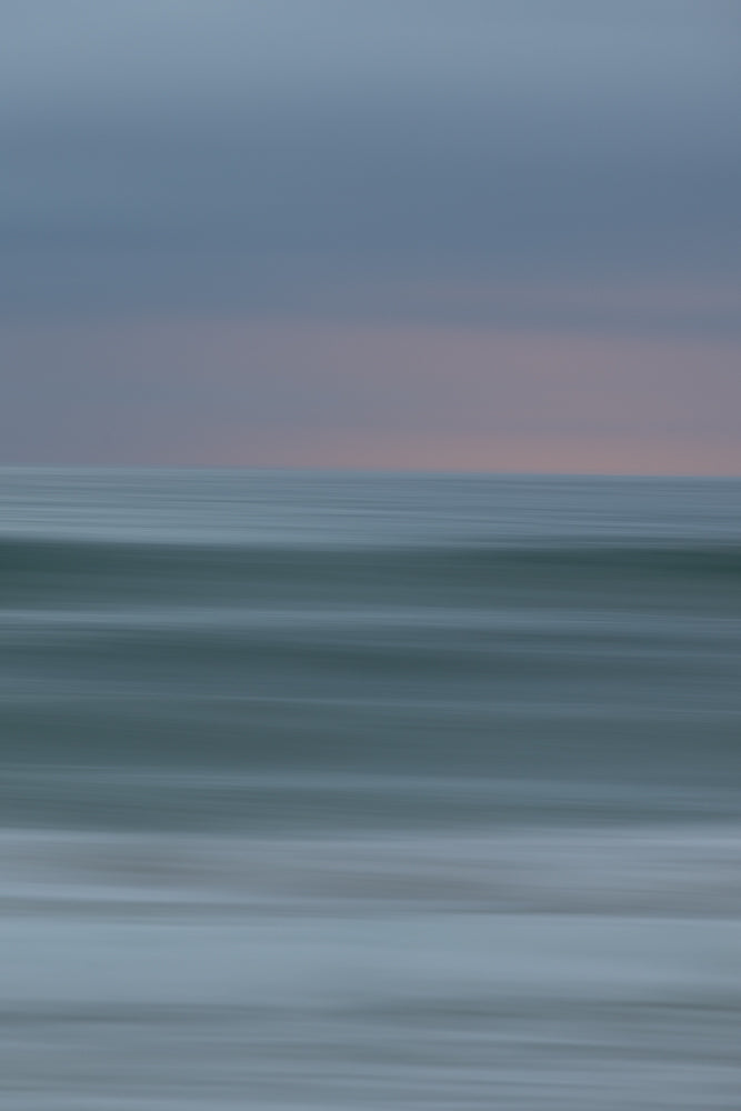 Abstract image of the ocean with horizontal lines of blue and grey, suggesting waves and sky at dusk.