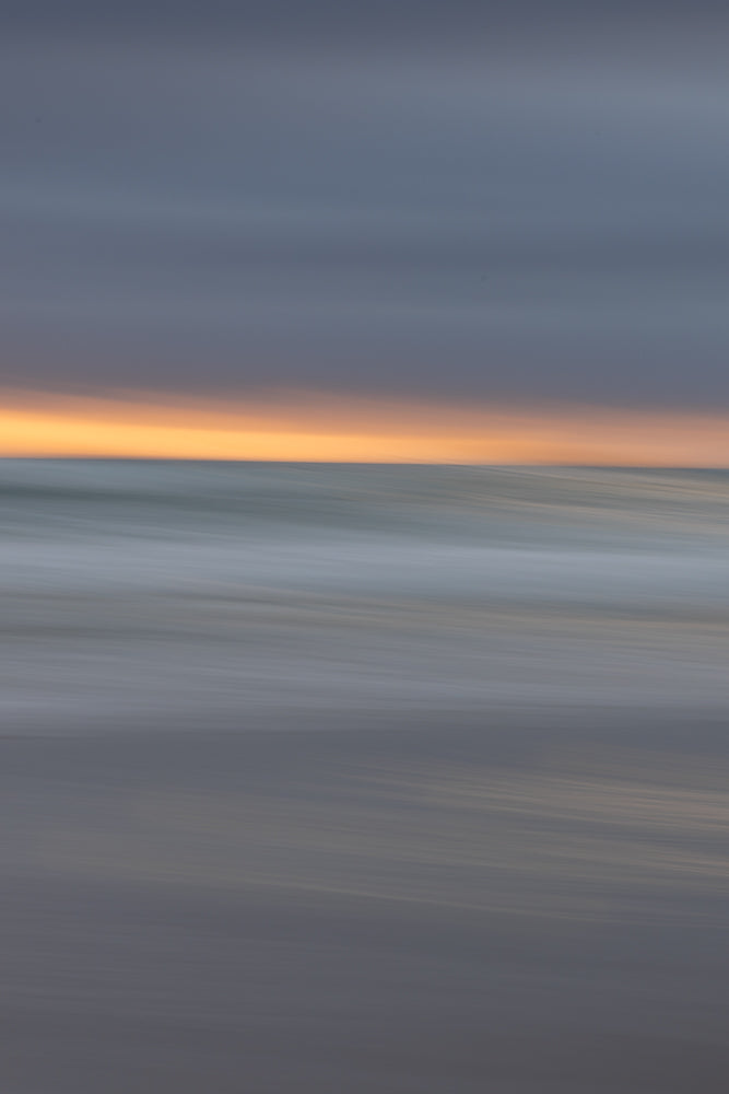 Abstract image of a beach at sunset with blurred horizontal lines of orange sky, grey ocean waves, and dark sand.
