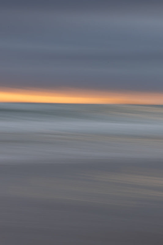 Abstract image of a beach at sunset with blurred horizontal lines of orange sky, grey ocean waves, and dark sand.