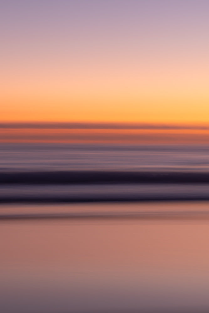 Abstract image of a sunset over the ocean. The sky transitions from pale purple at the top to soft orange and then a darker band of color. Below this, the ocean is depicted with horizontal bands of deep purple and lighter shades, reflecting the sky's colors.