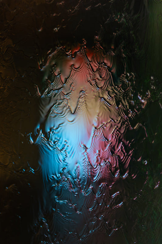 Abstract image of rippling water with red and blue lights reflecting on the surface. The water distorts the lights into wavy patterns.