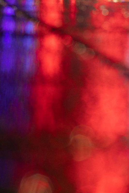 An abstract background with soft-focus bokeh lights in shades of deep red, bright red, and purple. The lights are blurred and out of focus, creating a dreamy and atmospheric effect.