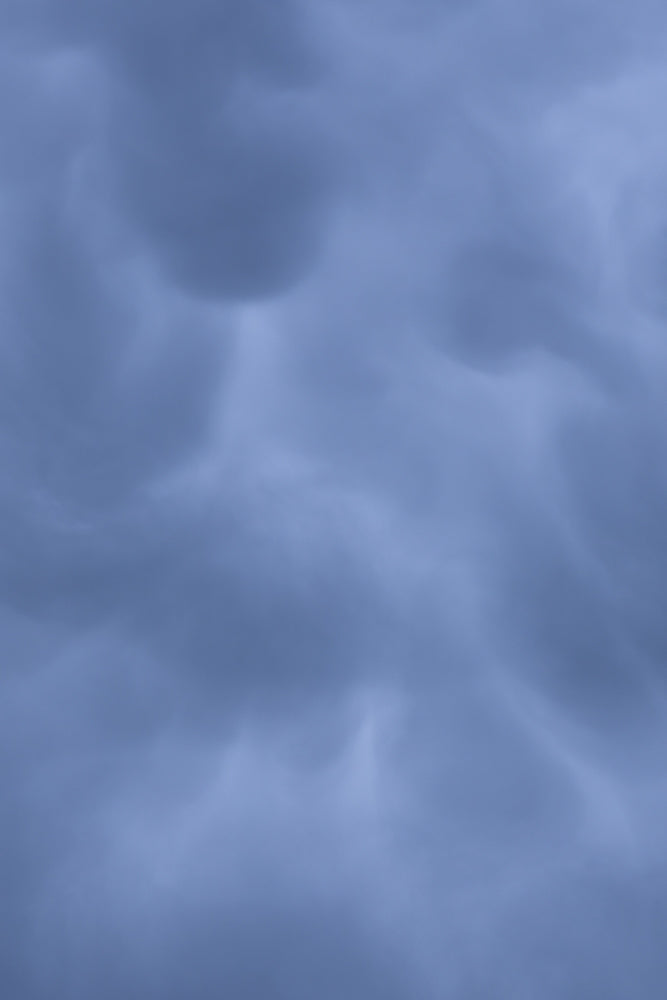 A close-up view of dark, ominous mammatus clouds against a pale blue sky, suggesting an impending storm.