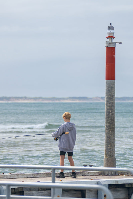 Boy fishing near a marker post at the end of the pier Barwon Heads