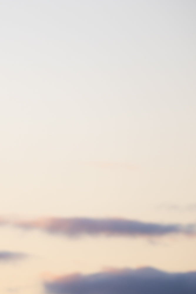 A soft focus image of a pale sky with wispy clouds in shades of pink and purple.