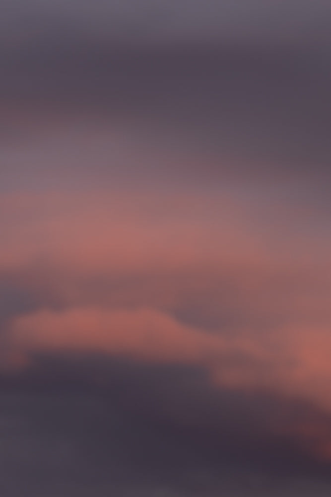 A soft focus image of clouds at sunset, with hues of pink and purple blending into a dusky grey sky.