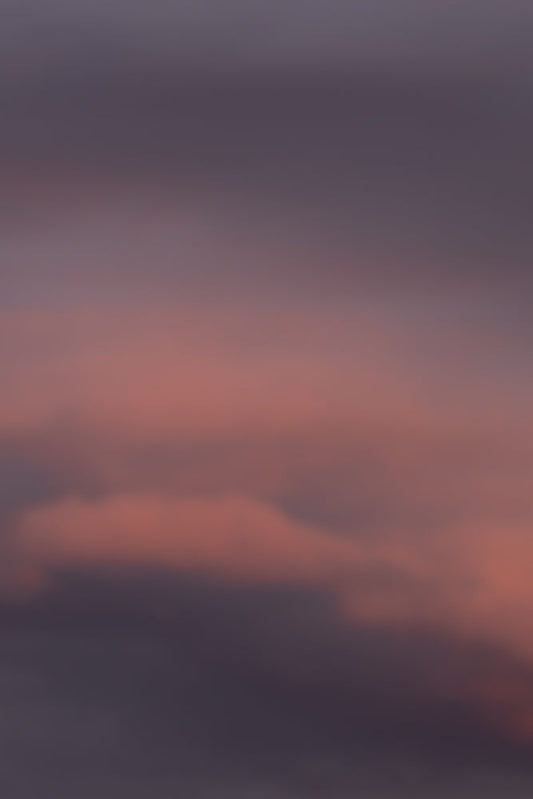 A soft focus image of clouds at sunset, with hues of pink and purple blending into a dusky grey sky.