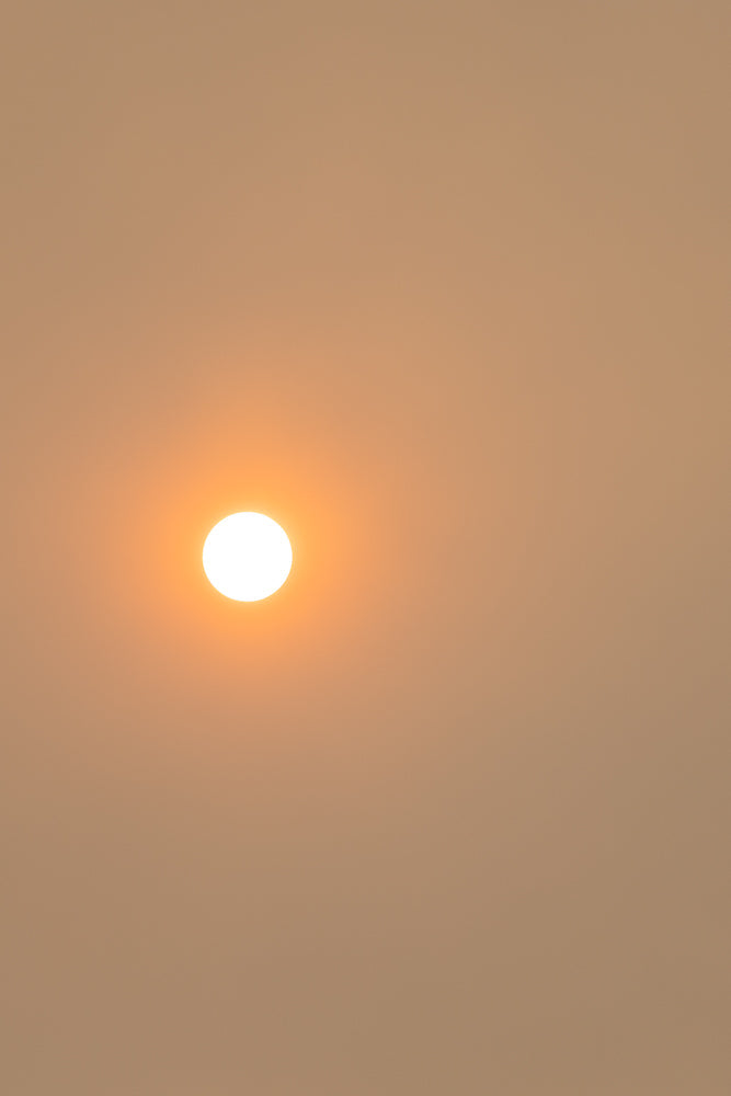 A bright, white sun is visible in the upper left quadrant of the frame, set against a hazy, pale orange sky. The sun is the primary focus, appearing as a perfect circle with a soft glow.