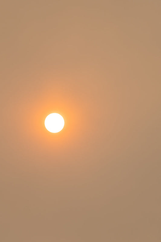 A bright, white sun is visible in the upper left quadrant of the frame, set against a hazy, pale orange sky. The sun is the primary focus, appearing as a perfect circle with a soft glow.
