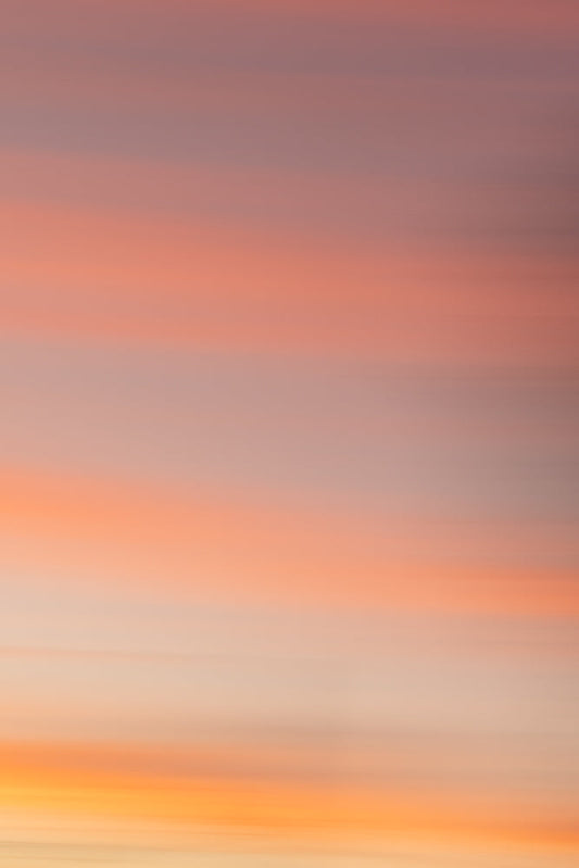 Abstract background of soft, horizontal bands of color transitioning from pale orange and yellow at the bottom to pink and muted purple at the top, evoking a serene sunset or sunrise.