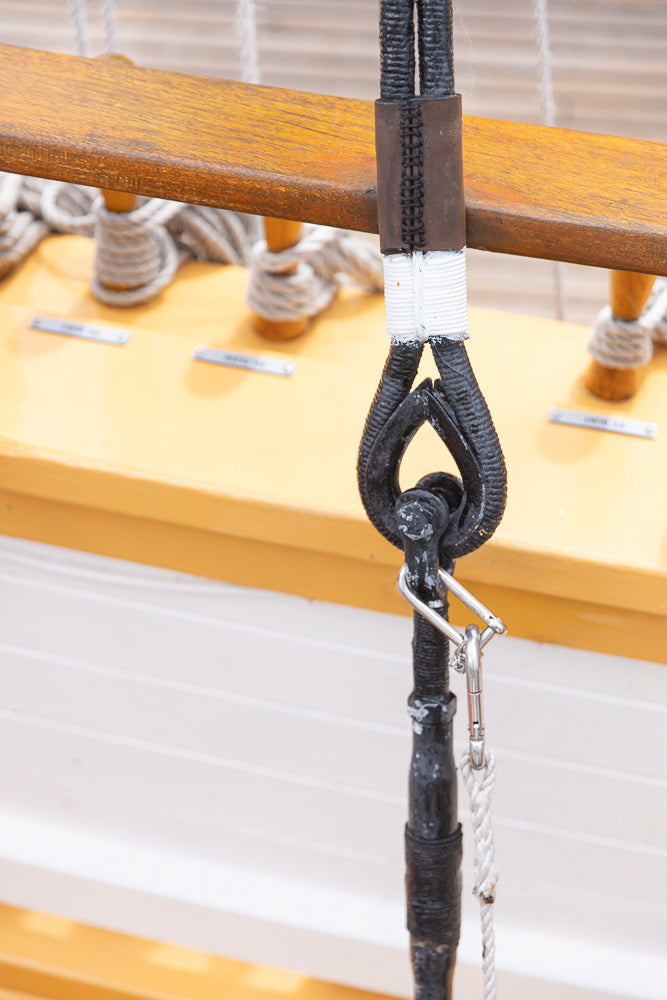 Close-up of a black metal shackle and rope attached to a wooden beam on a boat.