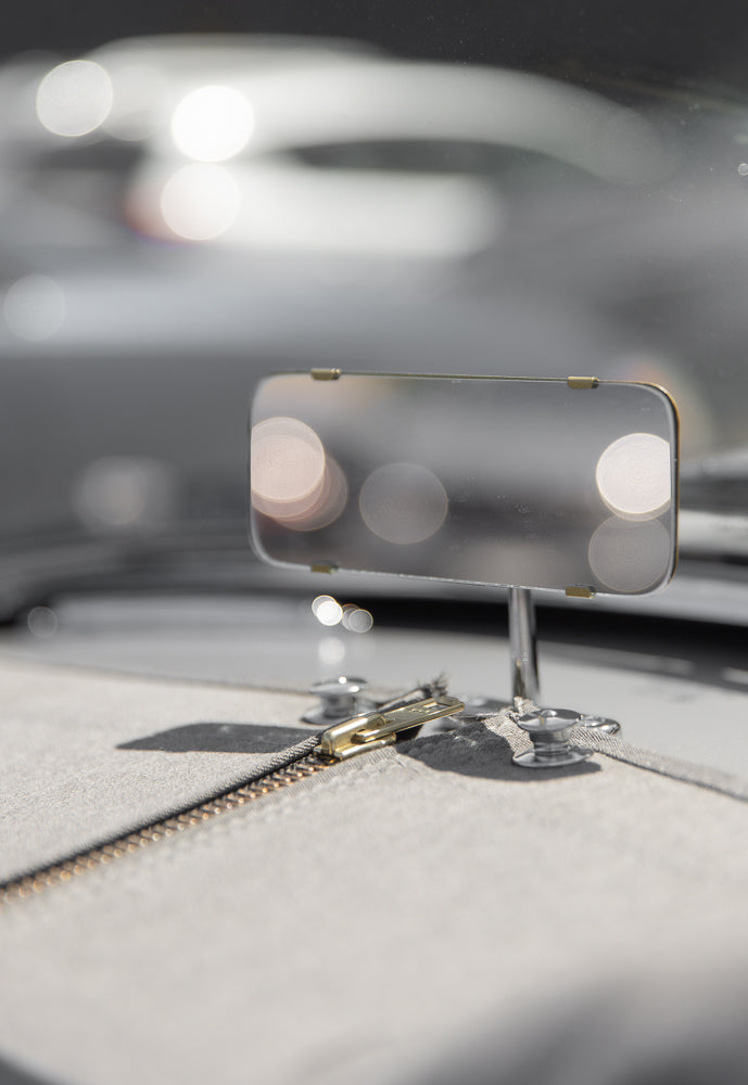 A close-up, shallow depth of field shot shows a gold zipper pull on a light gray fabric. The zipper is partially open, revealing the teeth. In the background, a reflective surface with bokeh lights is visible.