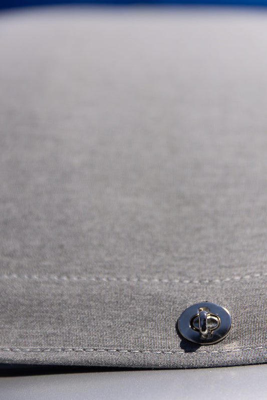 A close-up shot of a silver turn-lock closure on a gray fabric surface. The fabric has visible stitching and a textured weave. The background is blurred with a hint of blue at the top.