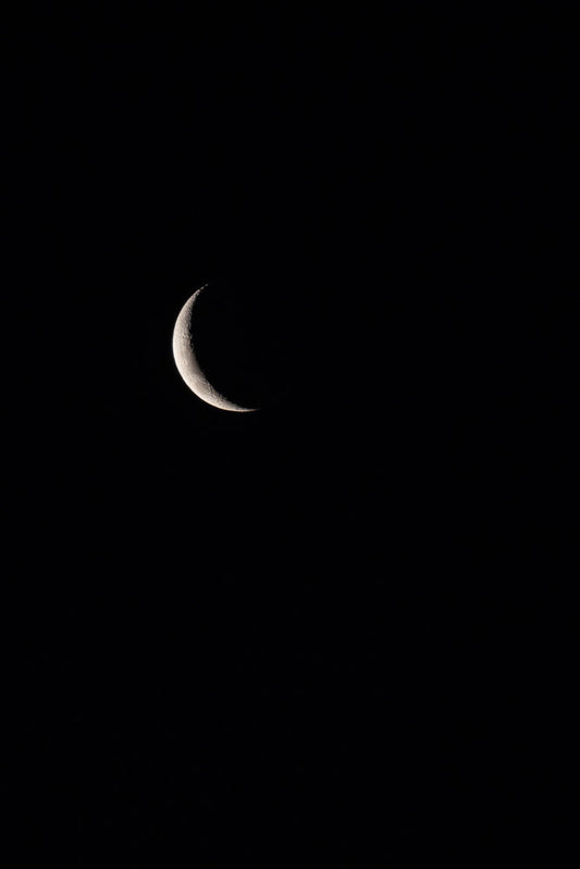 A crescent moon is visible against a completely black sky. The moon is illuminated from the right, showing its textured surface.