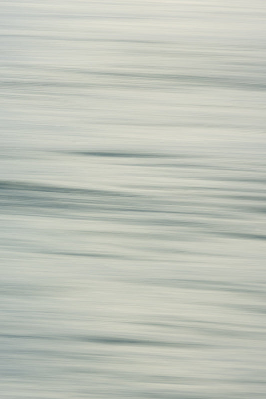 Abstract image of water with horizontal motion blur. The colors are muted blues and grays, creating a serene and calming effect.