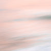 Abstract image of a beach at sunset with soft pink and peach tones blending into the pale blue of the ocean and white foam of the waves.