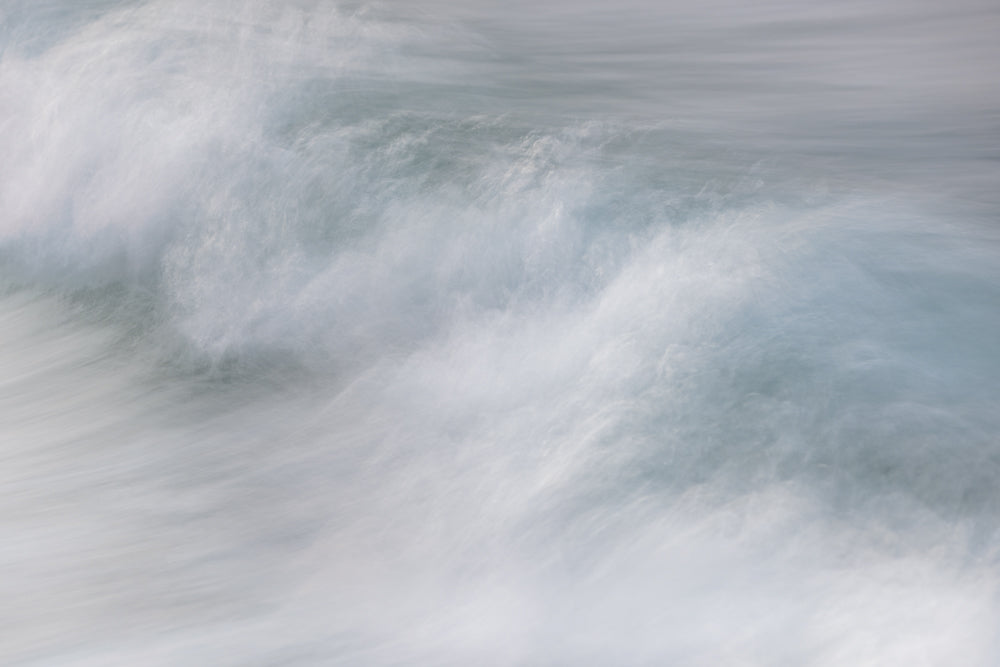 Abstract image of a wave with blurred motion, showing white foam and blue-grey water.