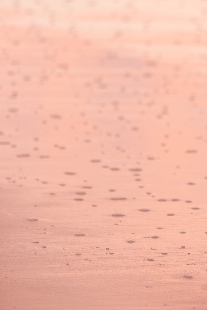A close-up, abstract shot of wet sand with small bubbles and ripples, illuminated by soft, warm light, creating a serene and textured background.