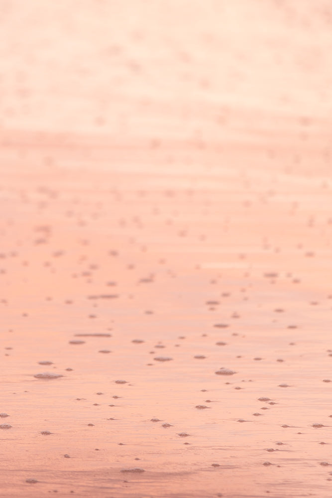 A close-up, abstract shot of wet sand with small bubbles and ripples, illuminated by soft, warm light, creating a serene and textured background.