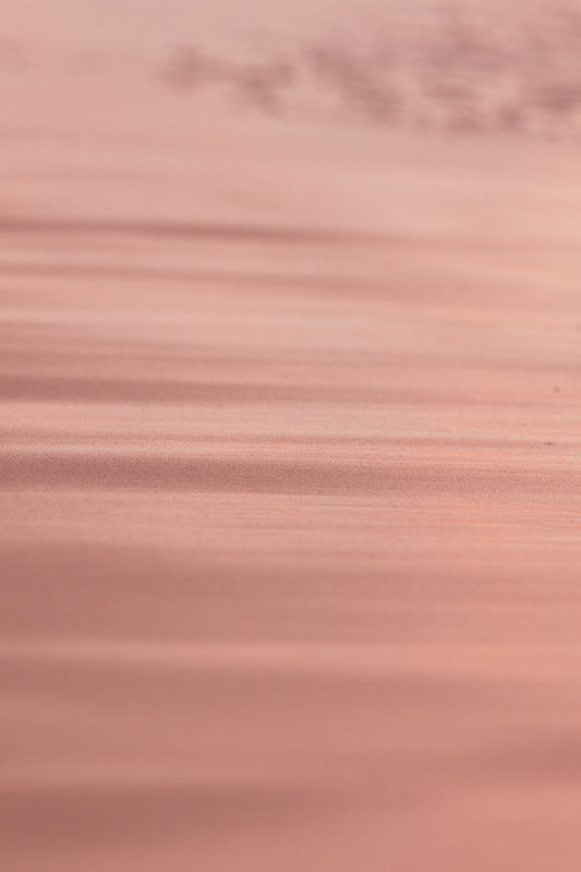 A soft focus, abstract background with horizontal lines of light and shadow in shades of rose gold and pink. The texture appears slightly grainy, creating a subtle, shimmering effect.